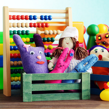 Sprachtherapeutisches Ambulatorium Eine Nahaufnahme verschiedener Spielzeuge in kleinen bunten Holzkisten. Man sieht Stoffpuppen, eine Gummiente, Spielfiguren und einen Abakus mit bunten Holzperlen.